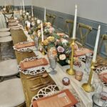 A fully designed table top for wedding reception featuring gold modern taper candle holders, ivory flameless candles and a lush floral design